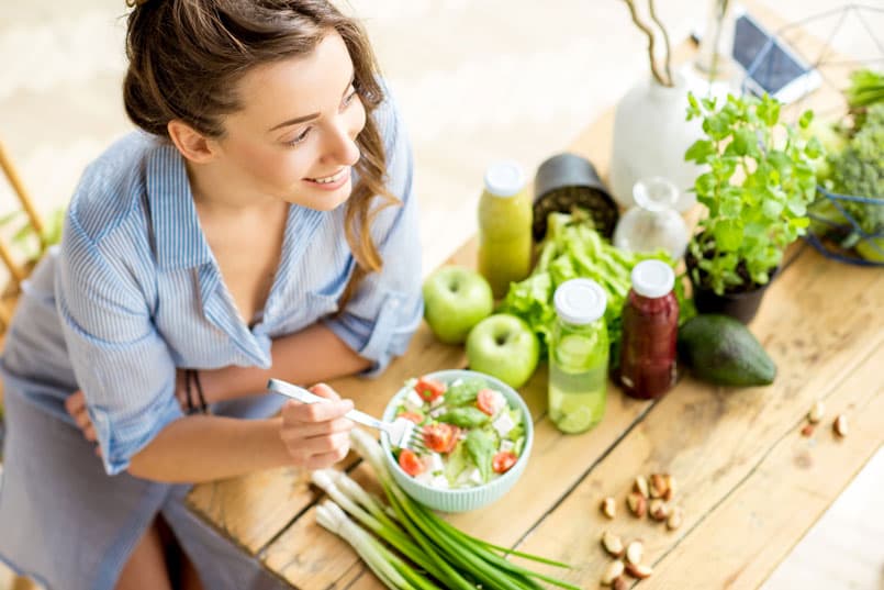 Smiling woman eating a healthy salad with fresh vegetables and juices, preparing for her first colonic at Amber Colonics in Tempe, AZ