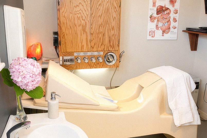 Colon hydrotherapy room featuring the Open LIBBE System bed, control panel, and a clean, comfortable setup for client wellness and privacy.