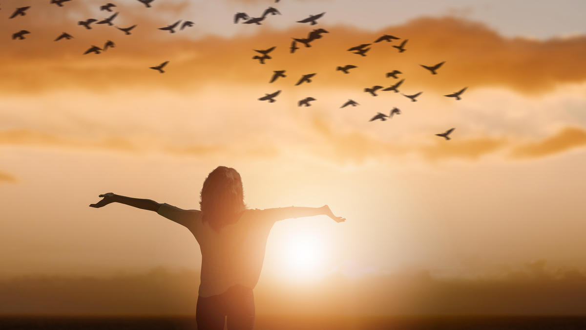 Person standing with open arms at sunrise with birds flying overhead, symbolizing freedom and vitality from Pulsed Electromagnetic Field (PEMF) Therapy Near Me