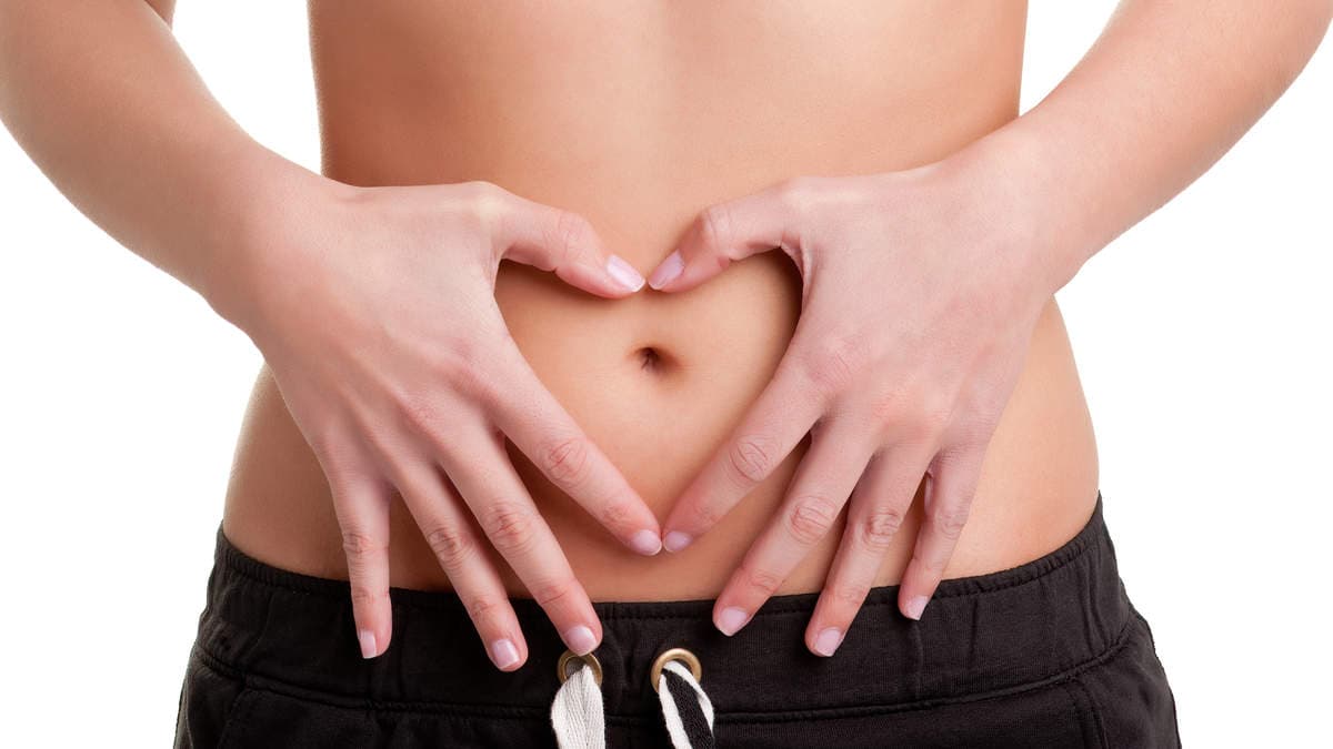Hands forming a heart over the lower abdomen, highlighting gut health for a colon hydrotherapy sessions guide.