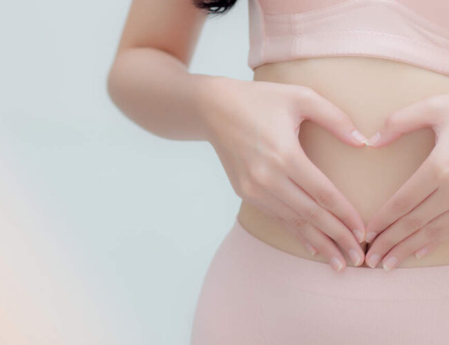 Hands forming a heart shape over the abdomen, symbolizing digestive comfort, gut health awareness, and bloating relief.