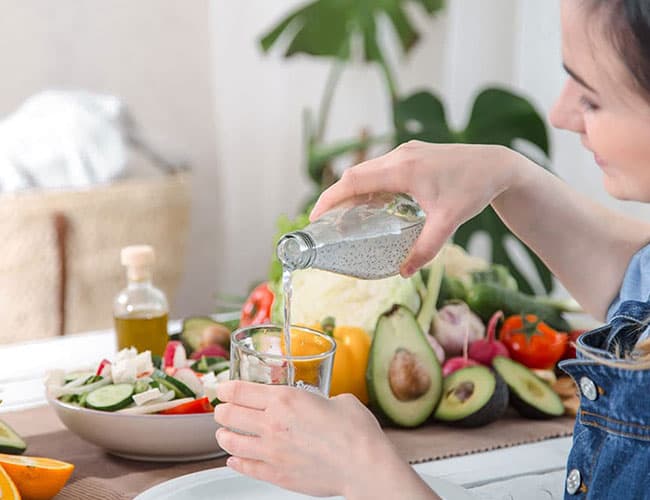 Woman relaxes in an infinity pool overlooking the ocean, representing PEMF-style relaxation for digestive comfort.