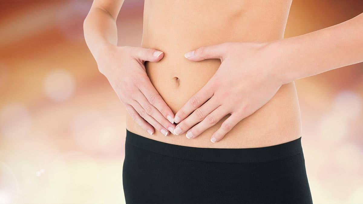 Woman holding lower abdomen to represent colon hydrotherapy, digestive wellness, and self-care support at Amber Colonics