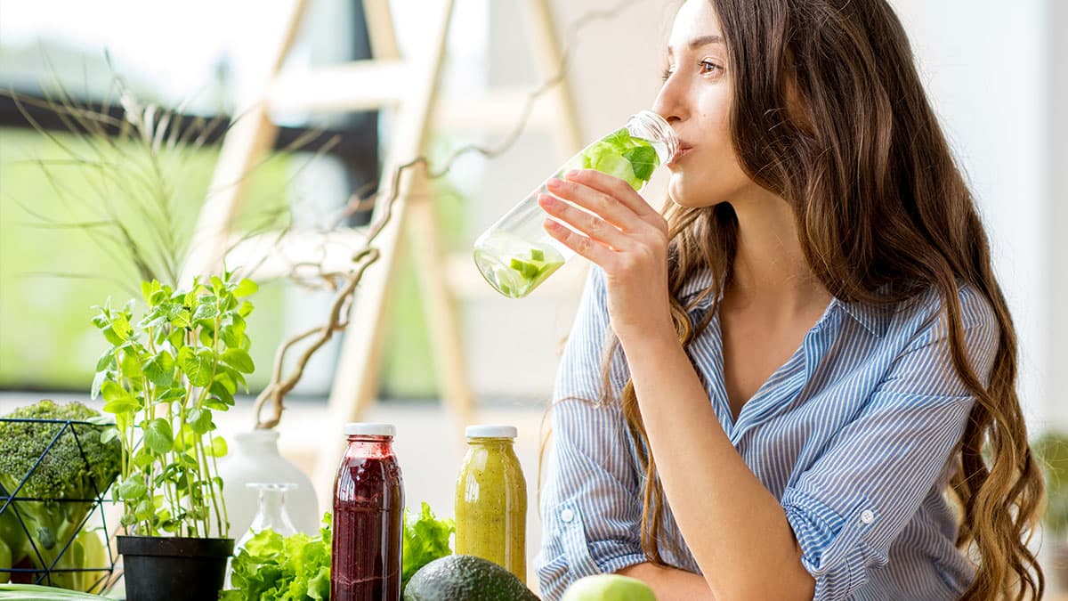 Woman drinking infused water with fresh greens for a Mesa and Gilbert digestive reset routine