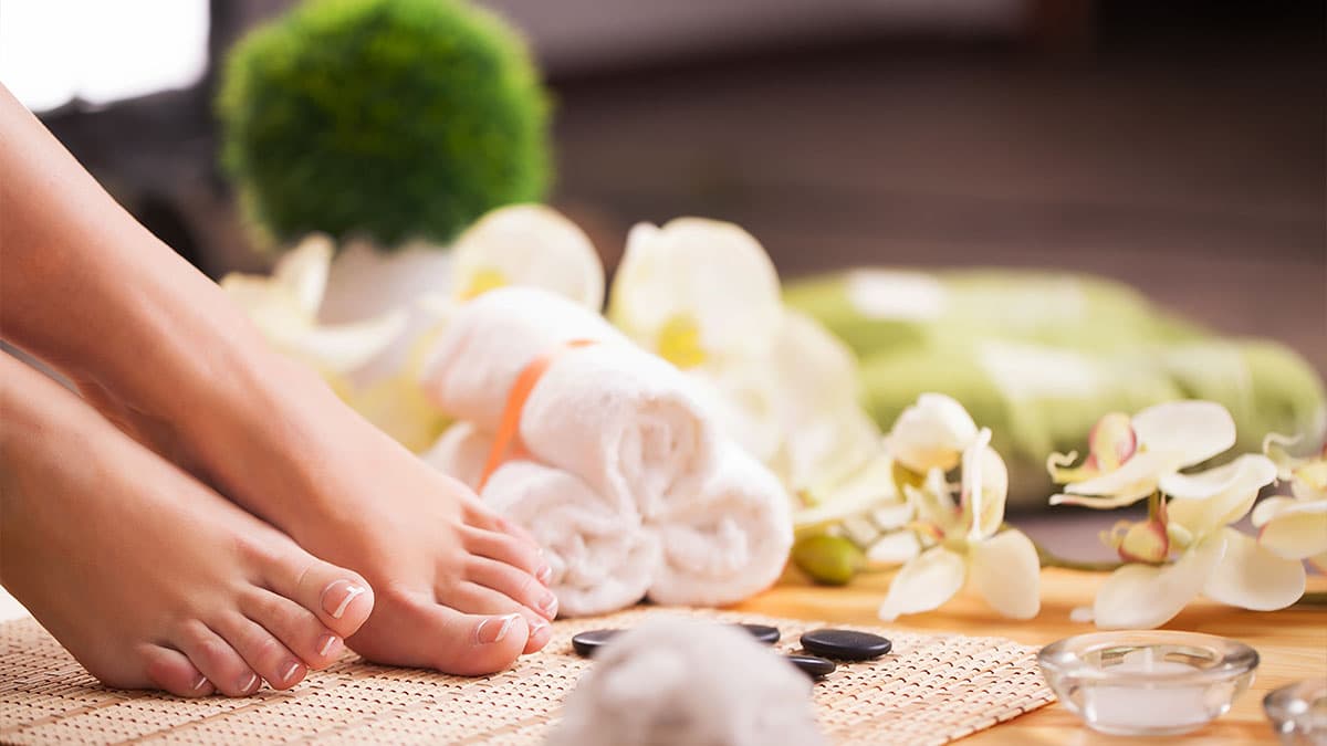 Bare feet beside towels, spa stones, and orchids, representing an Aqua-Ionic Foot Spa wellness visit in Tempe.