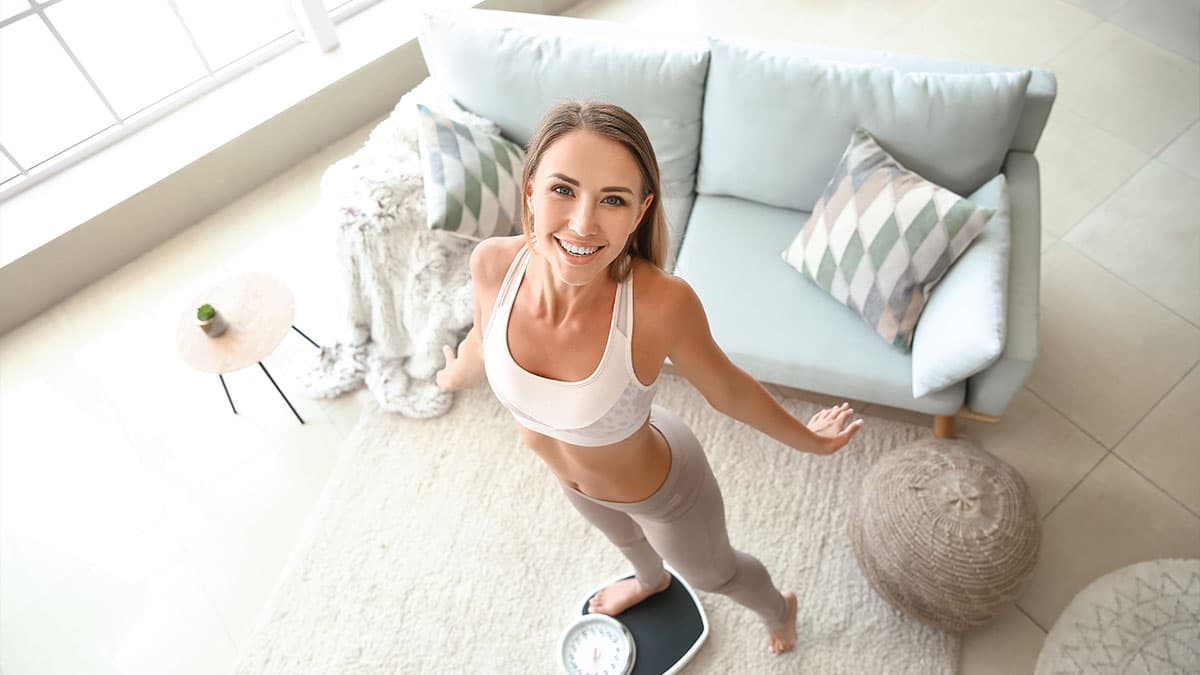 Smiling woman standing beside a scale in a bright living room